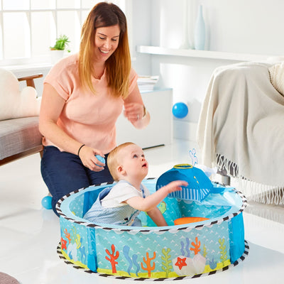 Baby playing in Kid Active Undersea Pop Up Sensory Ball Pit with whale launcher, supervised by adult in bright room.