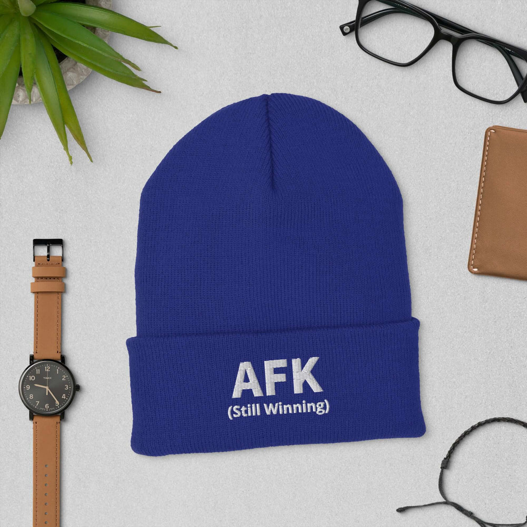 AFK Cuffed Beanie in blue color with 'Still Winning' text, styled with accessories and decor.